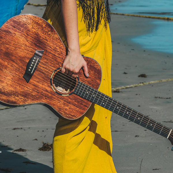 partial view of woman in yellow dress carrying acoustic guitar on beach