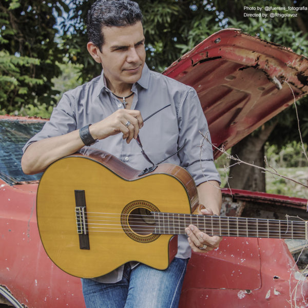 male musician leaning on red car holding Washburn acoustic guitar