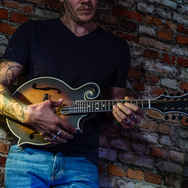 partial view of man in front of brick wall playing Washburn mandolin