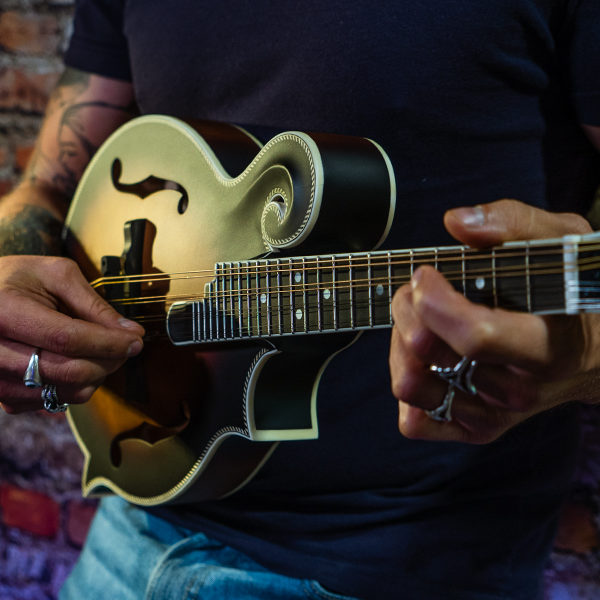 partial view of man in front of brick wall playing mandolin