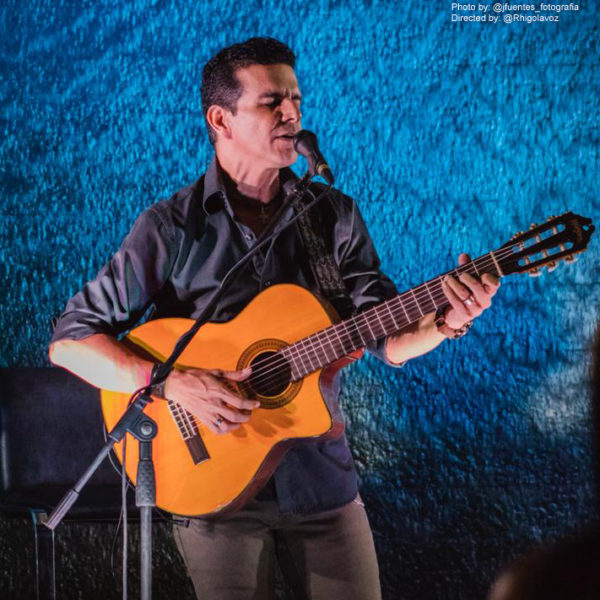 male musician playing Washburn classical guitar and singing in concert