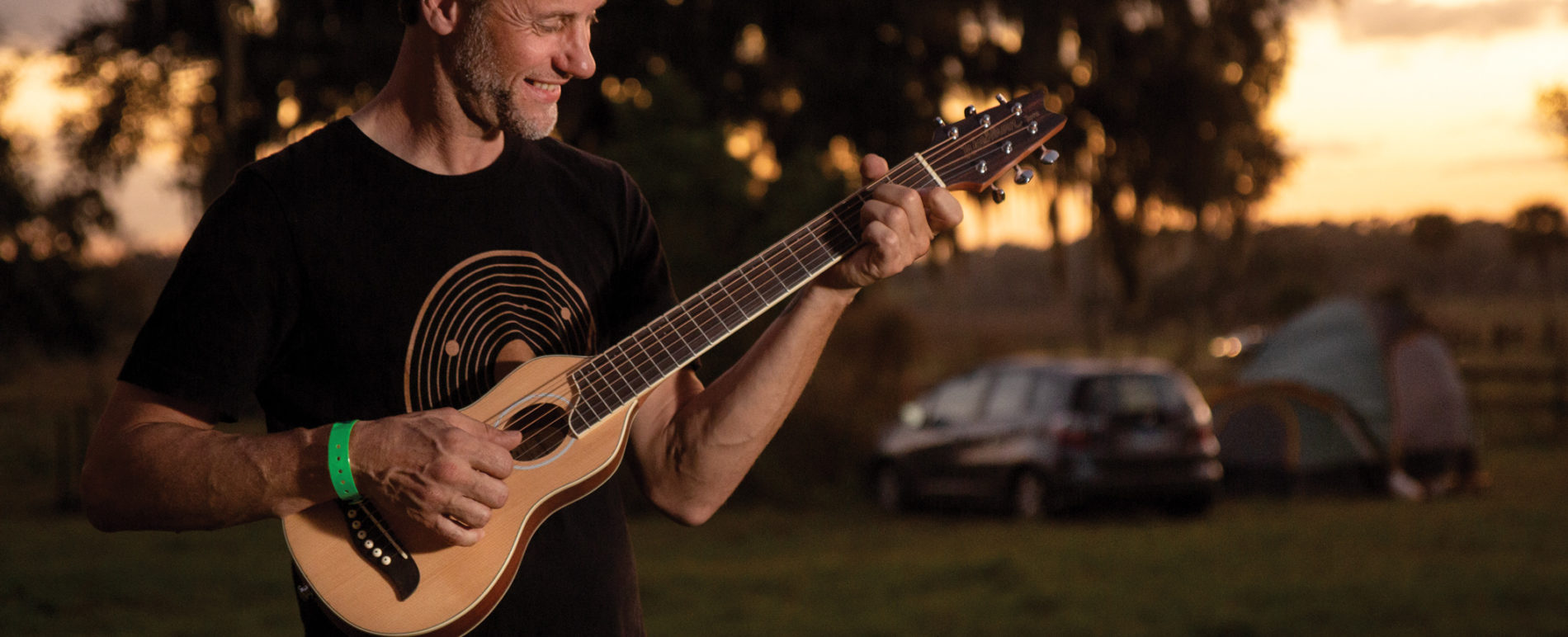 Artist playing RO10SK Rover Travel Guitar at a campsite