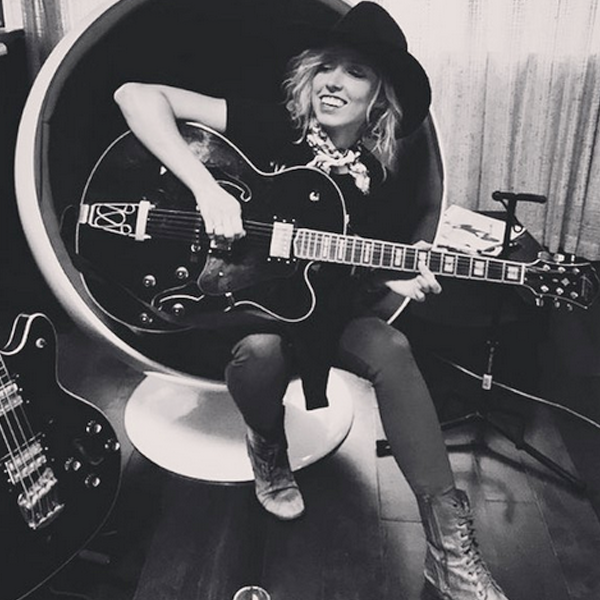 female musician playing black Washburn electric guitar in chair